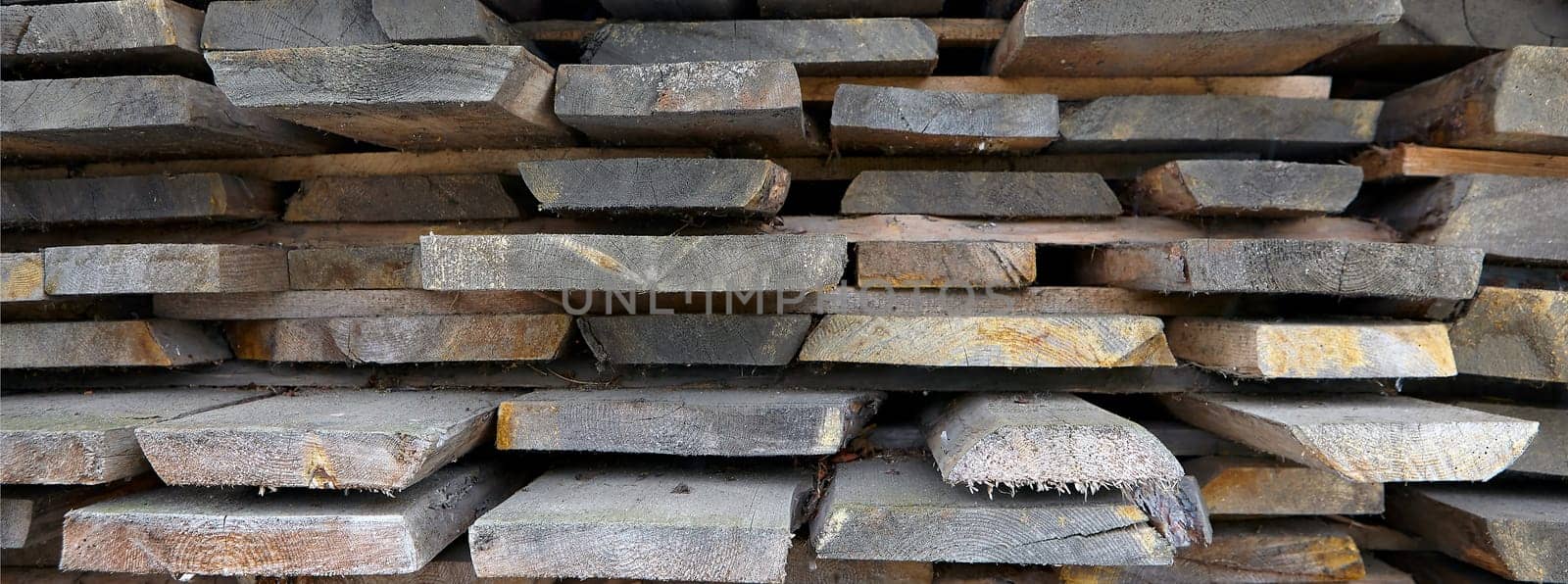 Folded in wooden piled beige beech boards, uneven bars background in a sawmill. Sawn-off boards