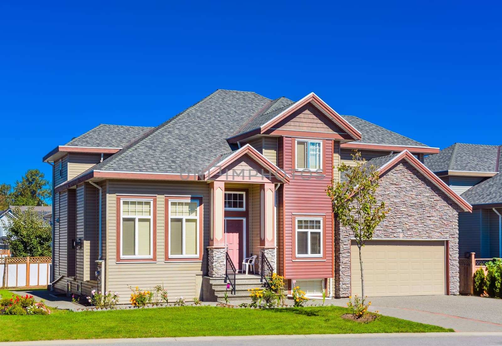New family house on sunny day with landscaped lawn in front and blue sky background. New house with concrete driveway and asphalt road in front.