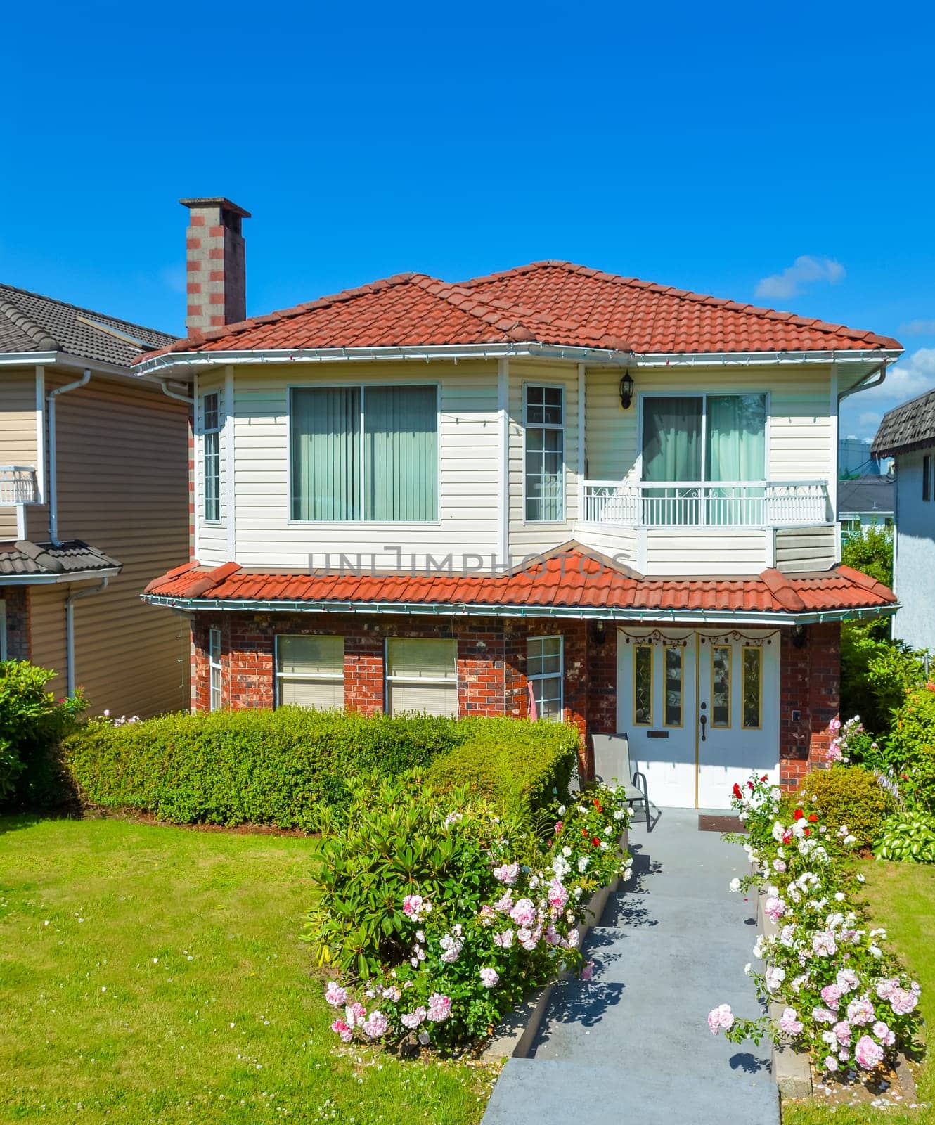 A perfect neighborhood. Average family house with concrete pathway to the entrance. Family residence on blue sky background