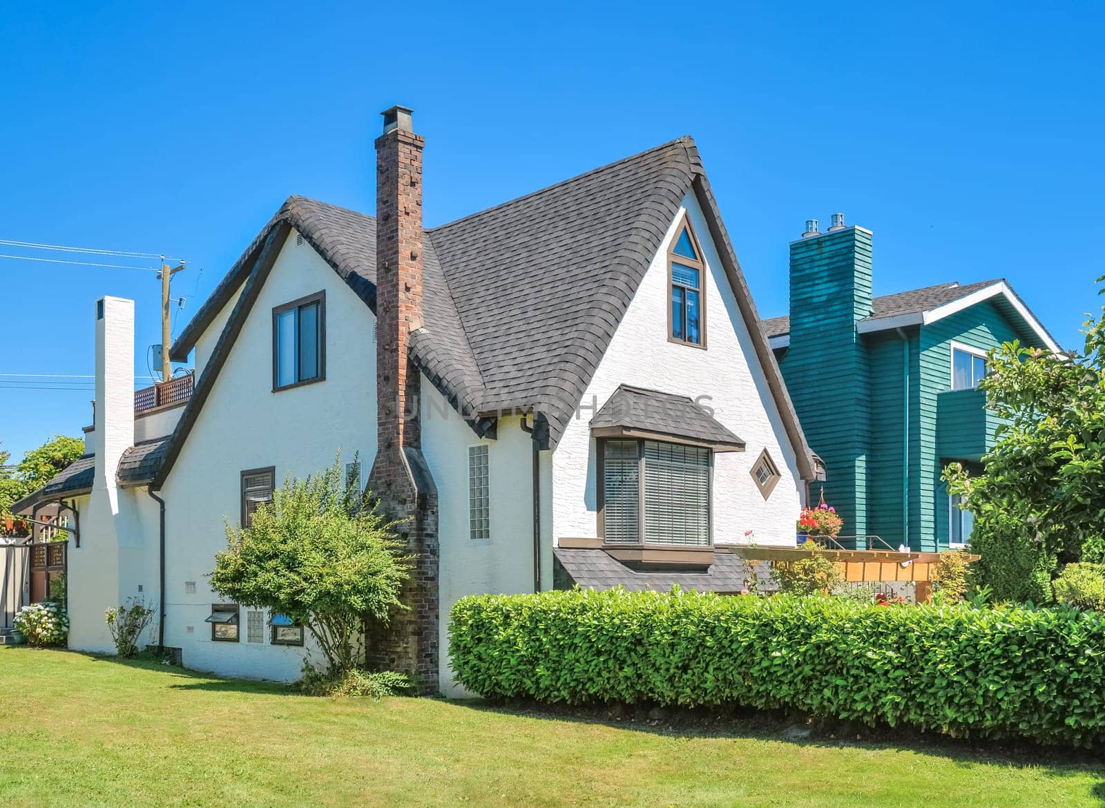 Old style family house with green lawn and hedgerow in front on blue sky background