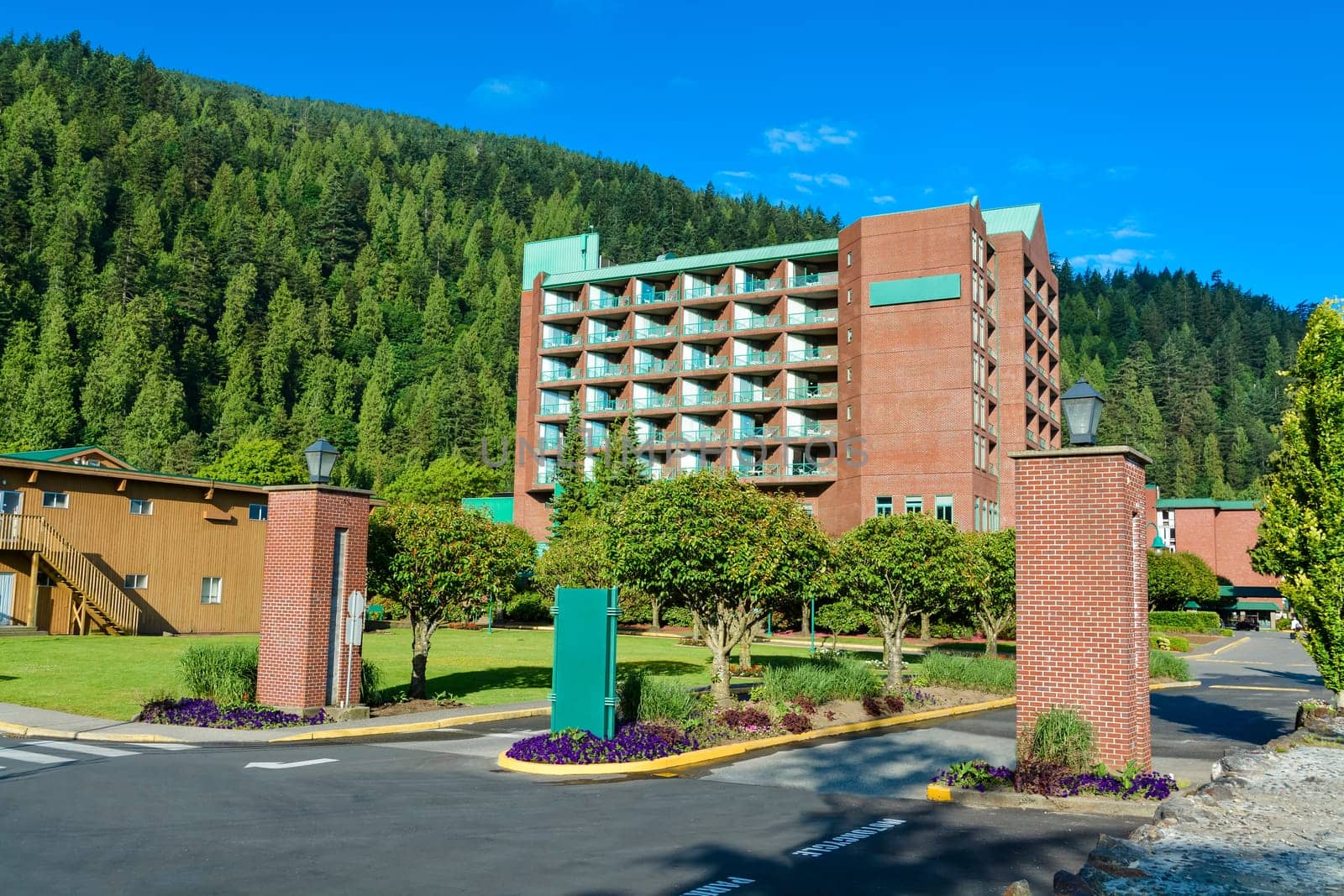Sand shore of the lake leading to resort building on green mountain and blue sky background