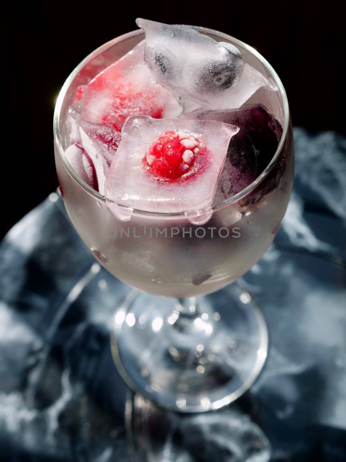 Glass with ice cubes with frozen berries and fruits close-up for a refreshing drink and preservation of seasonal vitamins raspberries, strawberries, cherries, blueberries, mulberries, blackberries