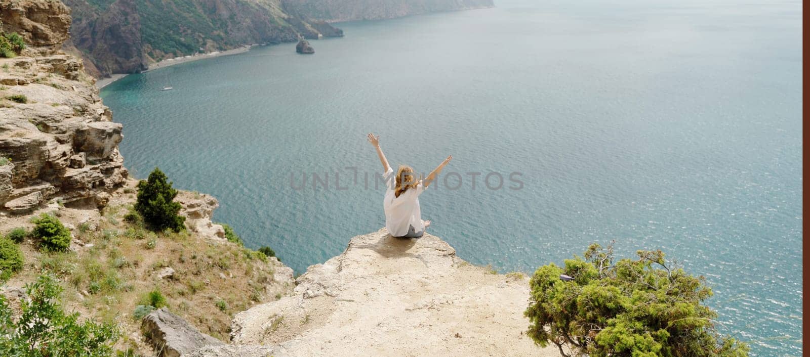 A woman is sitting on a rock overlooking the ocean. She is smiling and she is enjoying the view