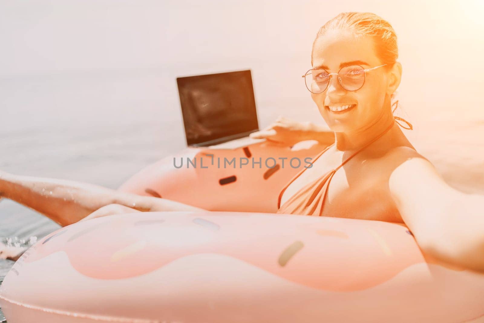 Woman laptop sea. Freelancer woman in sunglases floating on an inflatable big pink donut with a laptop in the sea. People summer vacation rest lifestyle concept