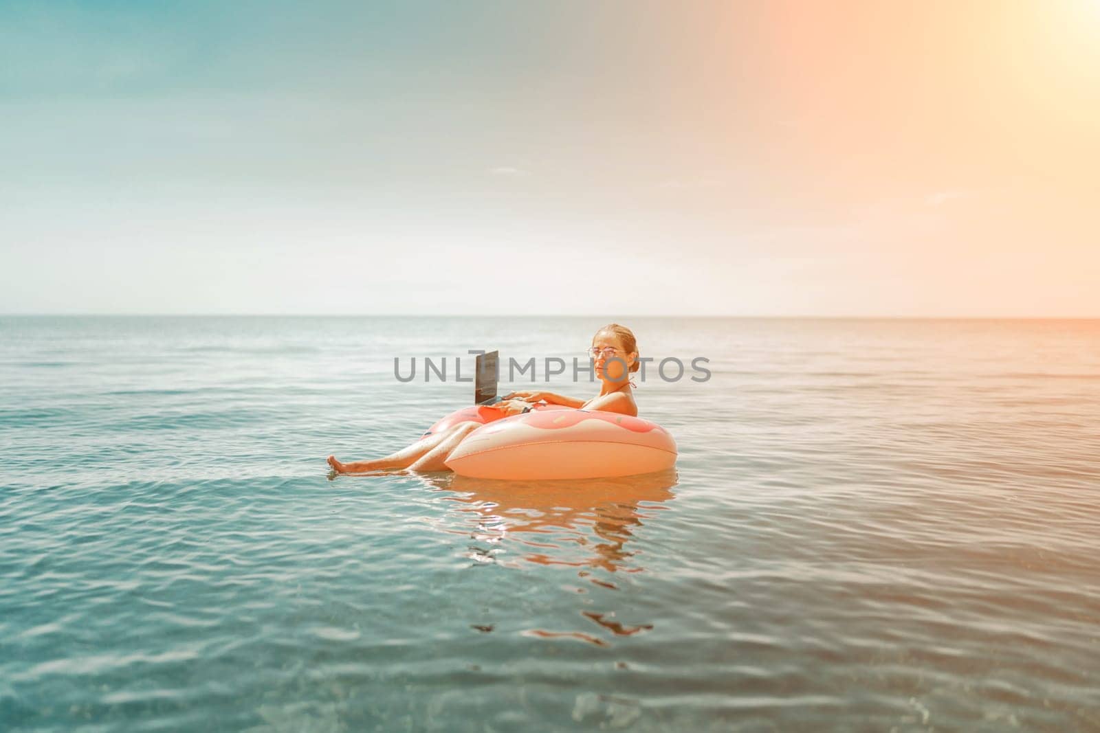 Woman laptop sea. Freelancer woman in sunglases floating on an inflatable big pink donut with a laptop in the sea. People summer vacation rest lifestyle concept