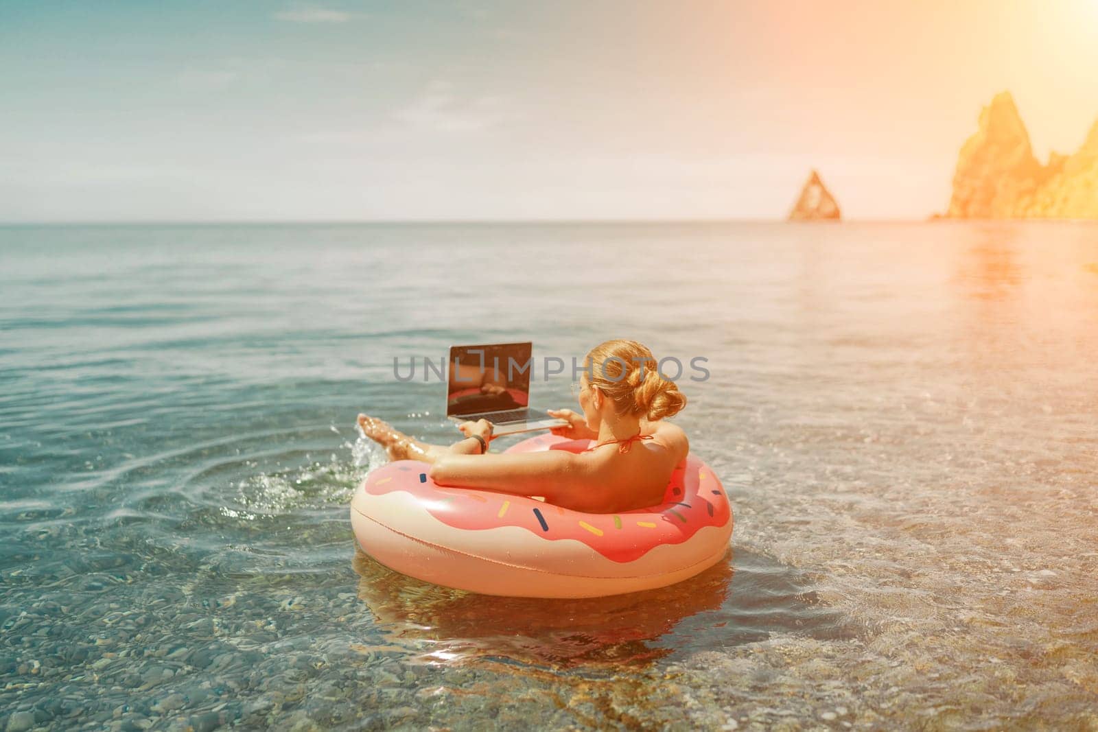 Woman laptop sea. Freelancer woman in sunglases floating on an inflatable big pink donut with a laptop in the sea. People summer vacation rest lifestyle concept