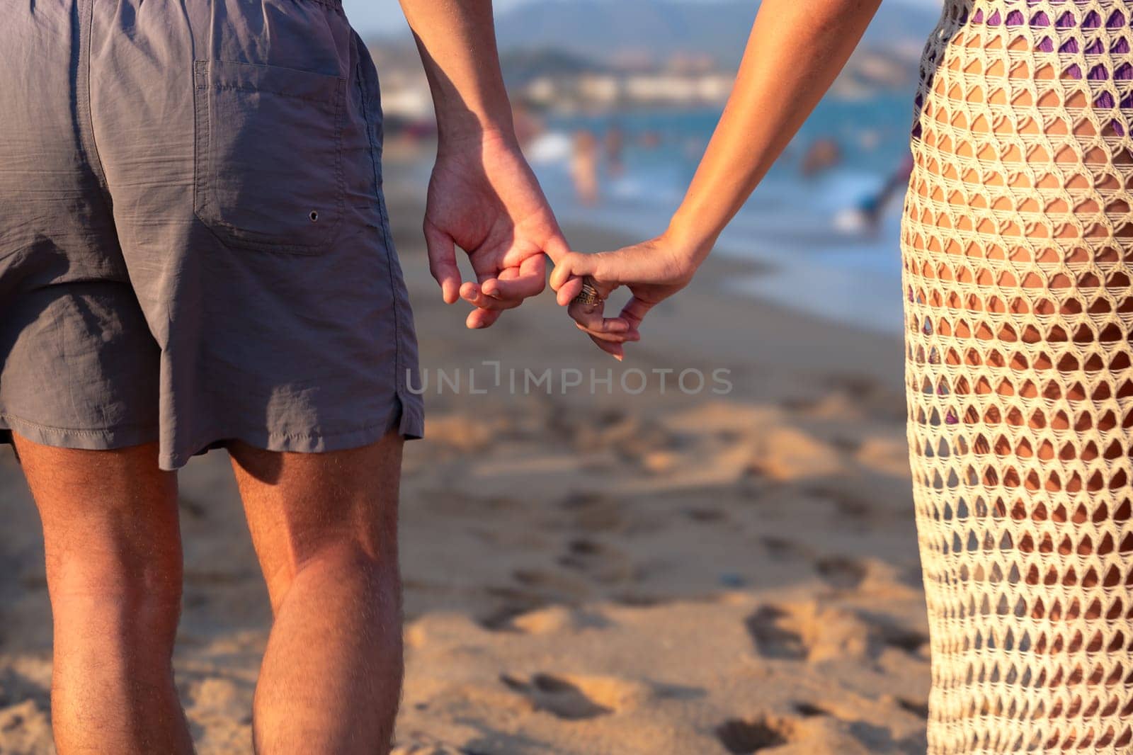 Happy couple in love holding hands and looking at each other on the seashore. A man and a woman are standing on the sand near the ocean. Vows and promises on the seashore.