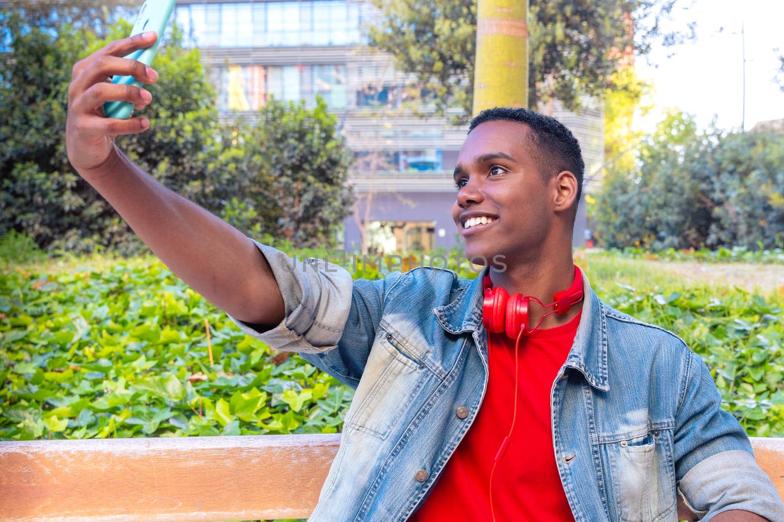 A happy student with headphones on the university campus taking a self-portrait to upload to a social media app