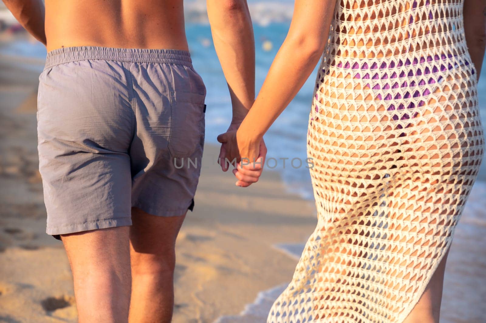 Happy couple in love holding hands and looking at each other on the seashore. A man and a woman are standing on the sand near the ocean. Vows and promises on the seashore.