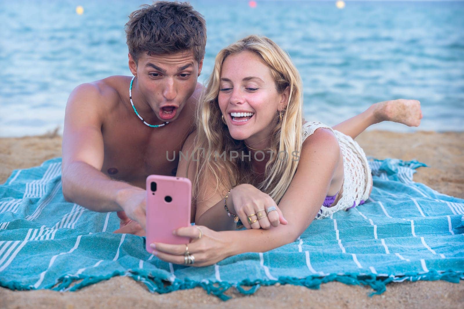 Man and woman hands typing on phone browsing social media phone sitting on beach
