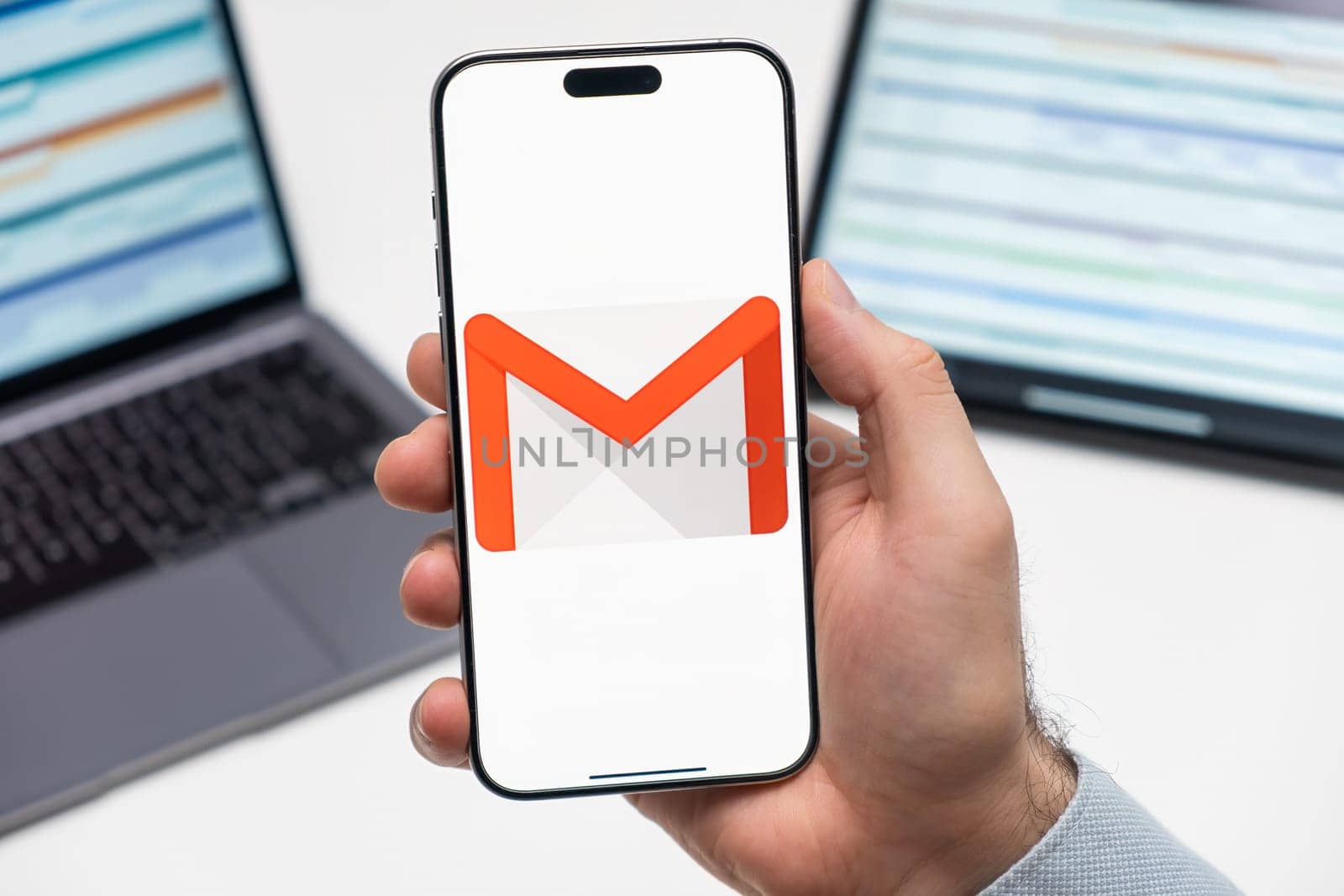 PRAGUE, CZECHIA - JULY, 2024: Gmail logo on the screen of smartphone in mans hand and laptop on the background