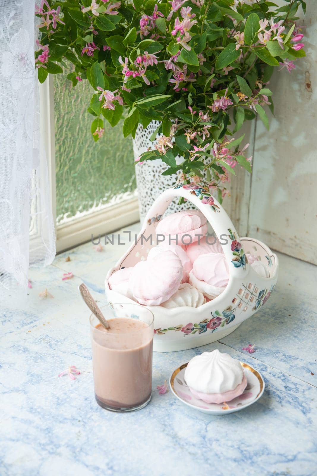 tender still life with full vase of vanilla marshmallows and glass of coffee with milk, next to vase with branches of pink flowers on wooden table, concept country lifestyle,