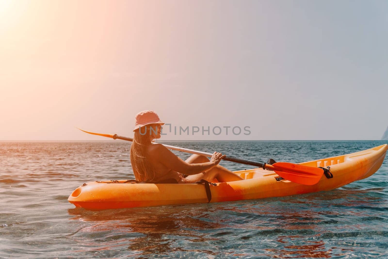 Happy smiling woman in kayak on ocean, paddling with wooden oar. Calm sea water and horizon in background