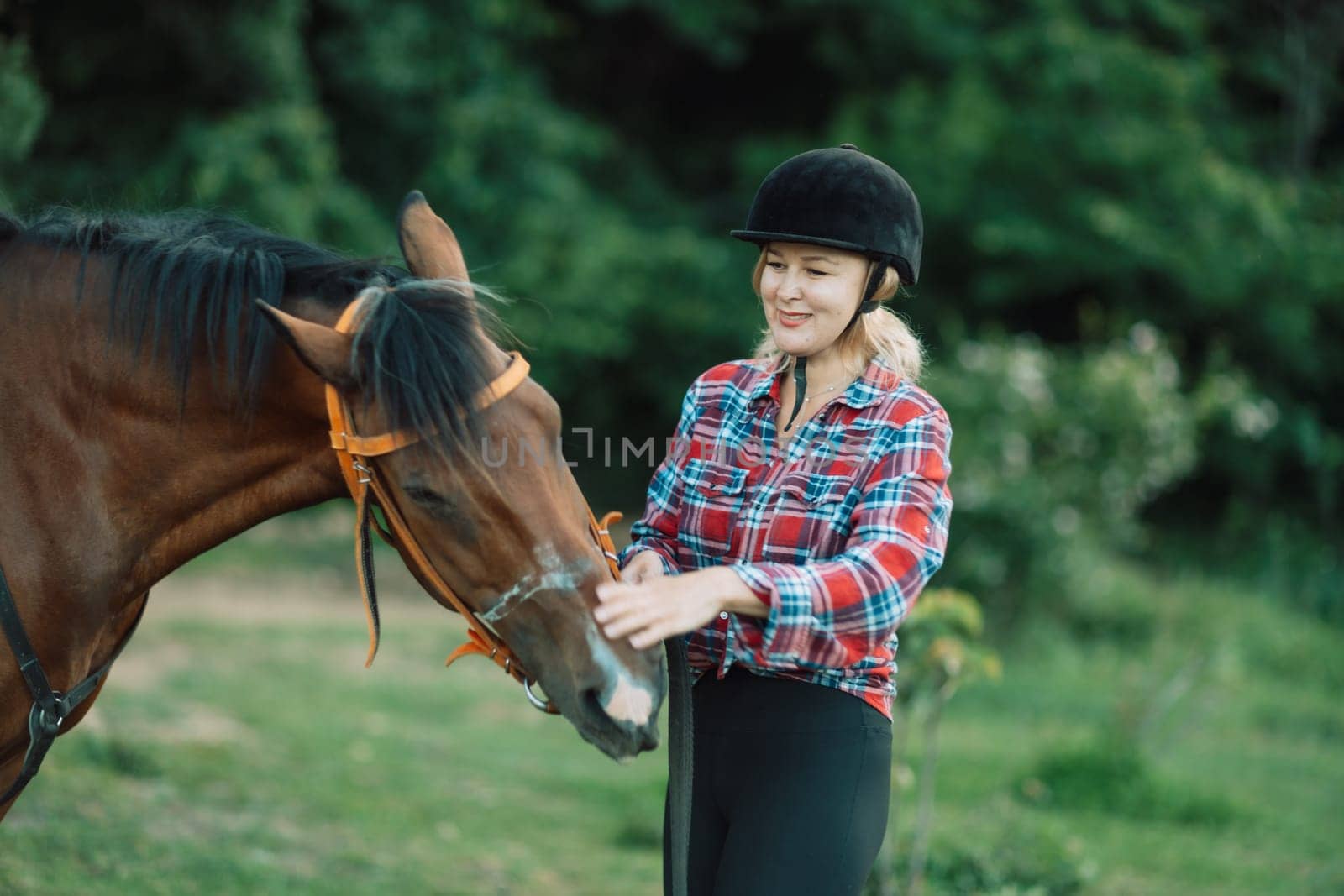 Happy blonde with horse in forest. Woman and a horse walking through the field during the day. Dressed in a plaid shirt and black leggings