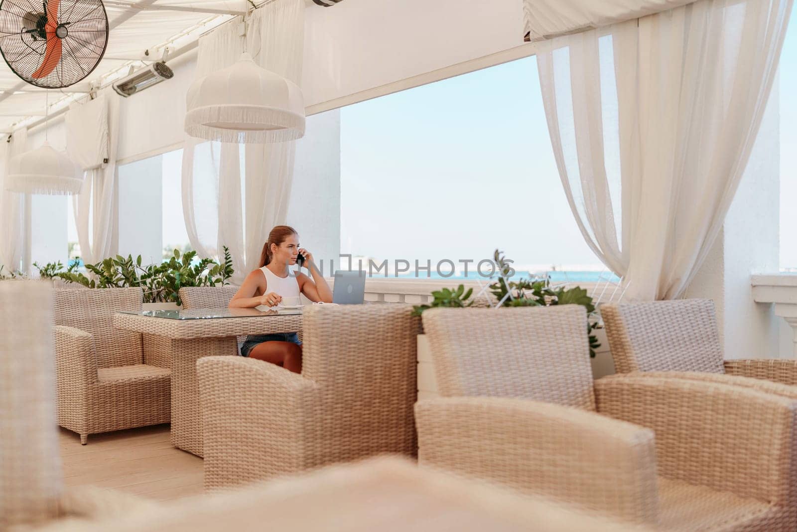 Woman coffee cafe laptop sea. Female freelancer using laptop on coffee break in modern cafe with sea view in the morning.