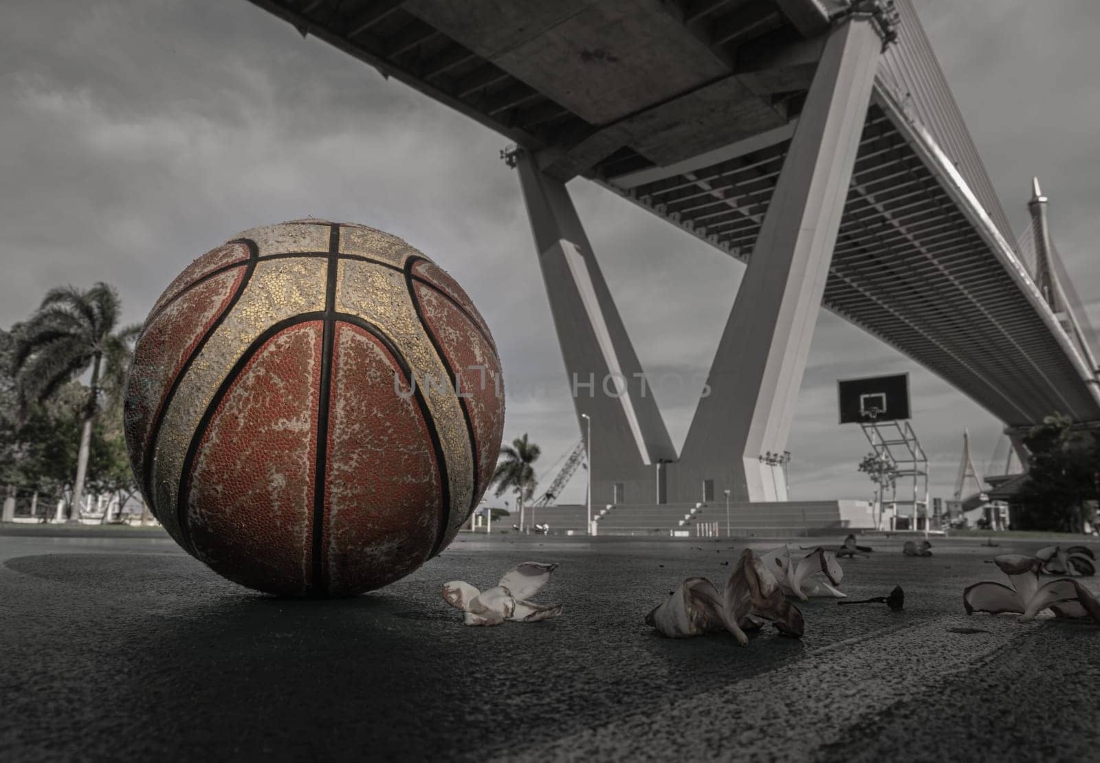 Basketball ball on the Old cement court floor at Outdoor park with Suspension bridge and Sky in the background. Space for text, Selective focus.