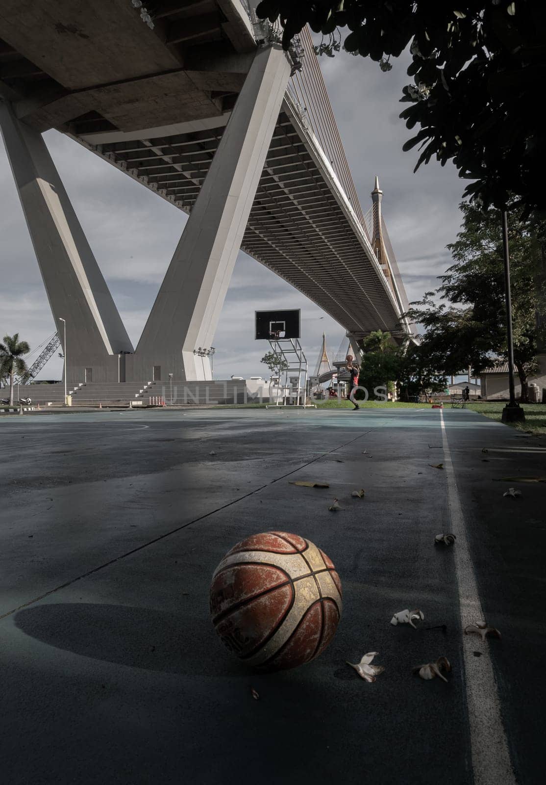 Basketball ball on the Old cement court floor at Outdoor park with Suspension bridge and Sky in the background. Space for text, Selective focus.