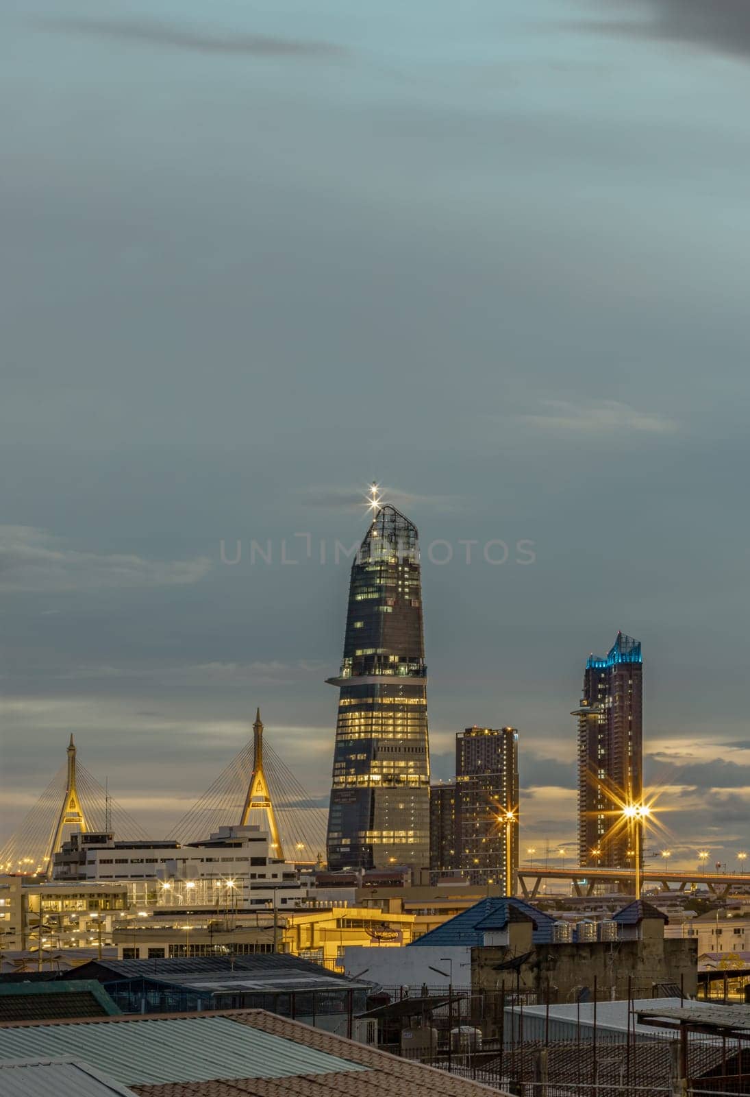 Bangkok, Thailand - Aug 14, 2024 - Night city view with KingBridge tower alongside the iconic landmark of Bhumibol Bridge. Stunning At Twilight skyline of bangkok business district with Skyscrapers use it as your wallpaper, poster and banner design, Selective focus.