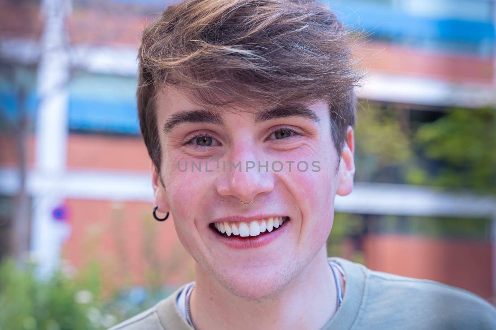 Positive young man in casual clothes smiling and looking at camera in cityscape.