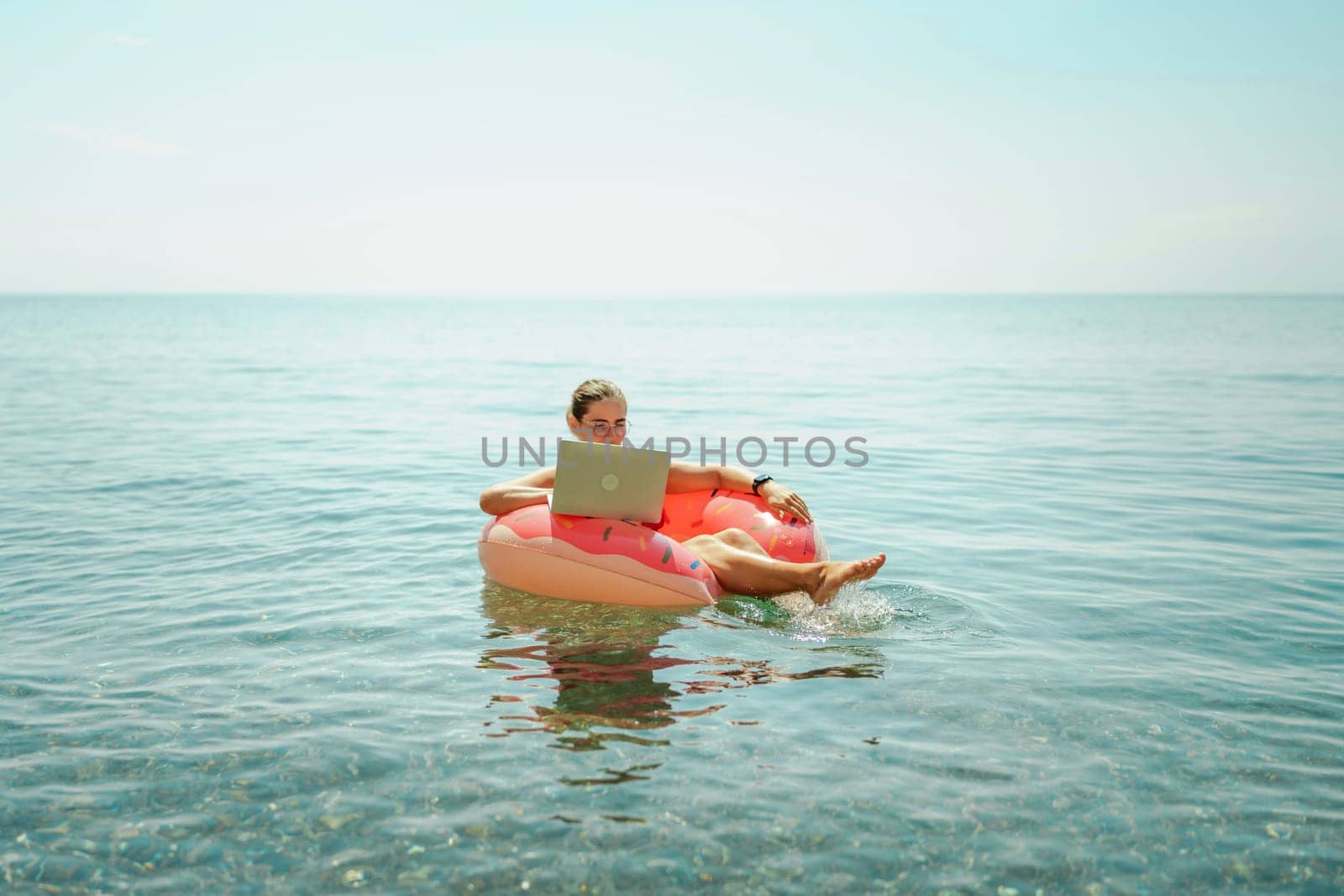 Woman laptop sea. Freelancer woman in sunglases floating on an inflatable big pink donut with a laptop in the sea. People summer vacation rest lifestyle concept