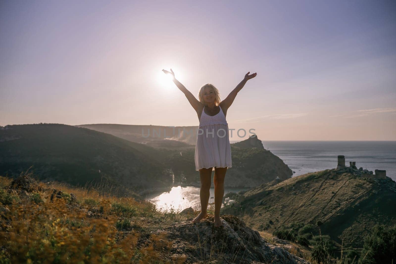 woman standing hill with her arms raised in the air, looking up at the sun. The scene is peaceful and serene, with the woman's expression conveying a sense of joy and happiness