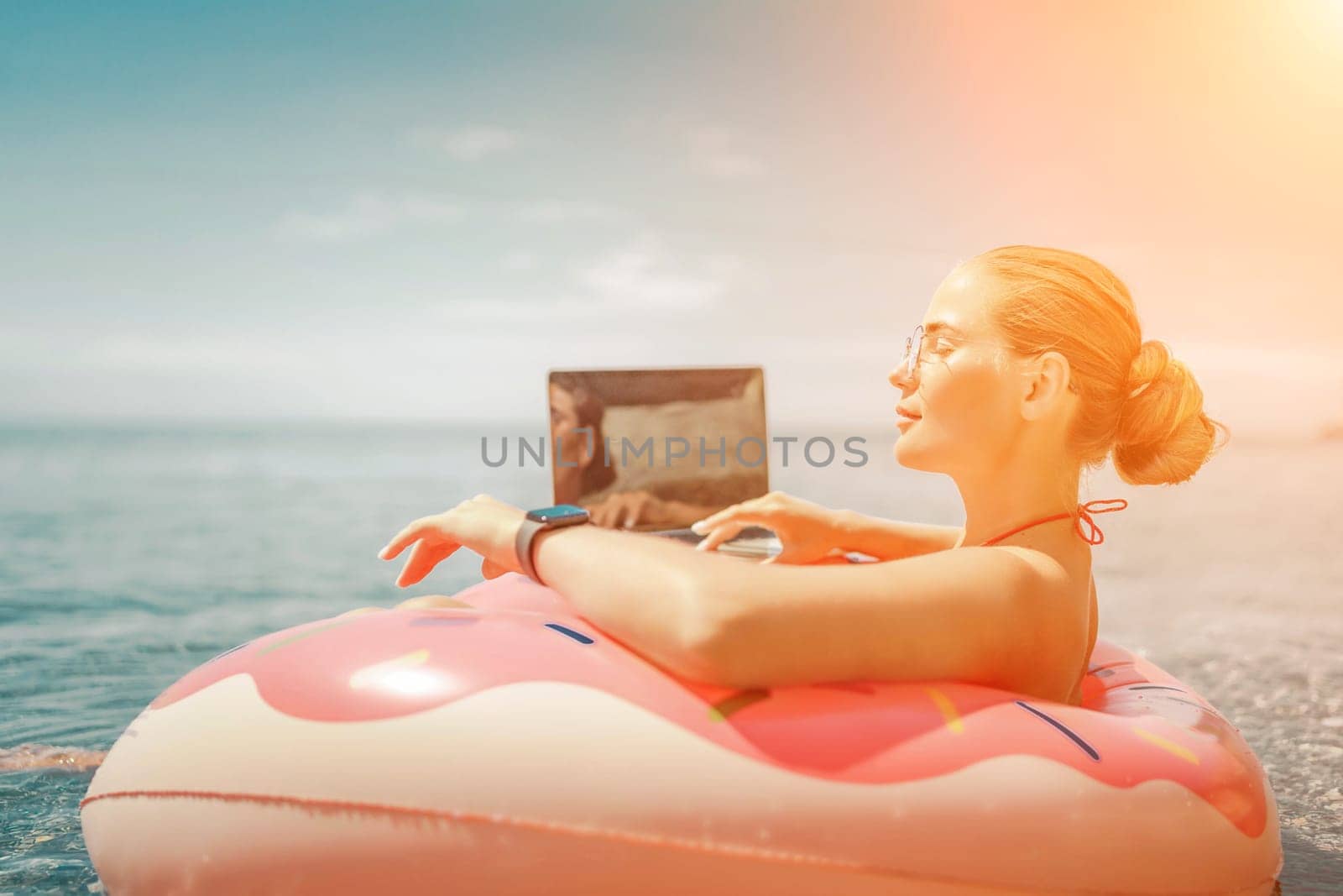 Woman laptop sea. Freelancer woman in sunglases floating on an inflatable big pink donut with a laptop in the sea. People summer vacation rest lifestyle concept