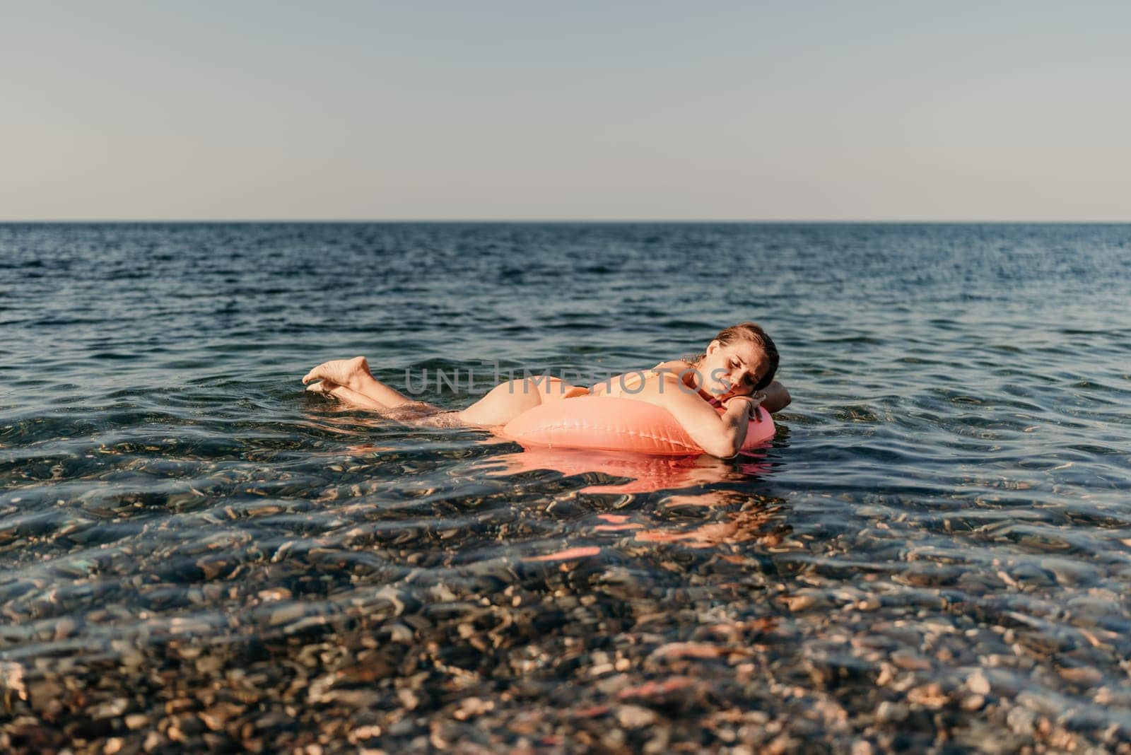 A woman is floating on a pink inflatable raft in the ocean. The water is calm and the sky is clear. The woman is enjoying her time in the water