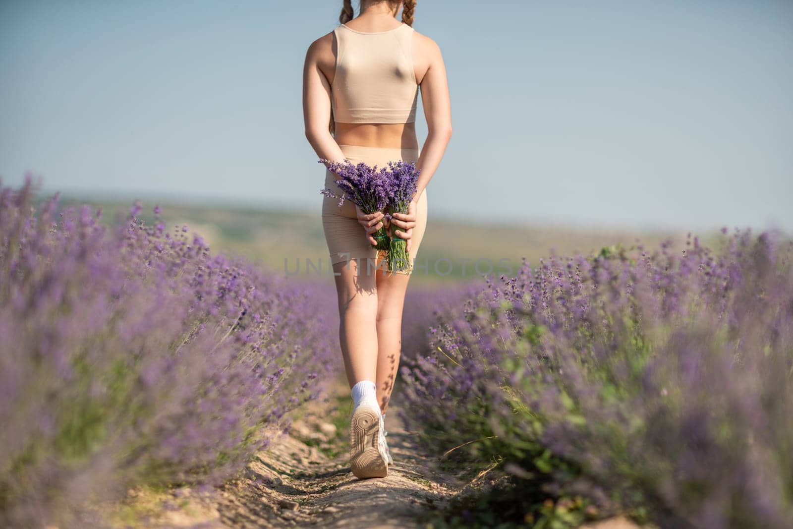 girl holding bouquet lavender flowers. The flowers are purple and the woman is wearing a tan top. Concept of calm and relaxation, as lavender is often associated with these feelings