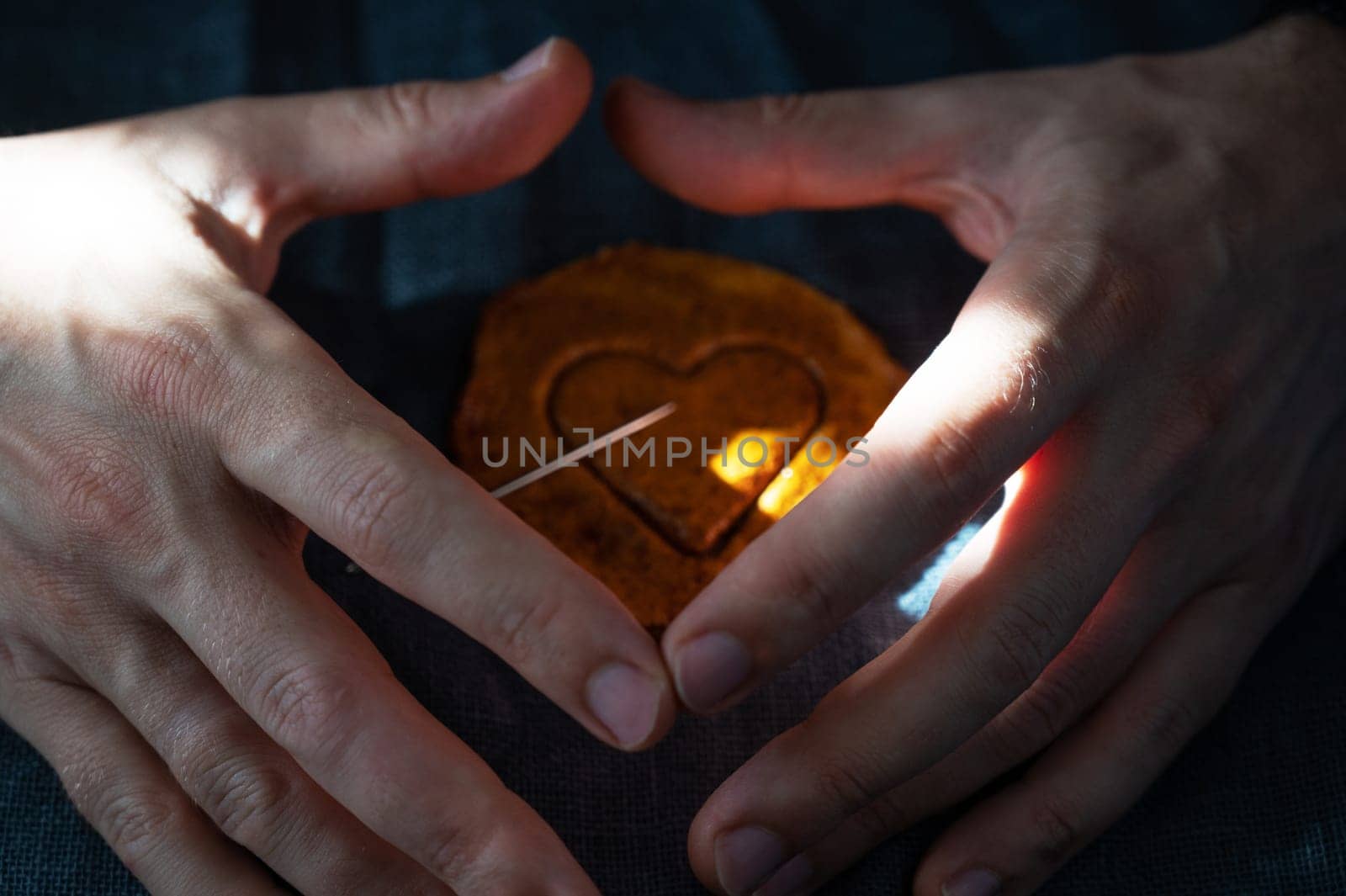 Men's hands closeup with brown sugar caramel candy cookies with a metal needle in the shape of a heart. Concept of survival game