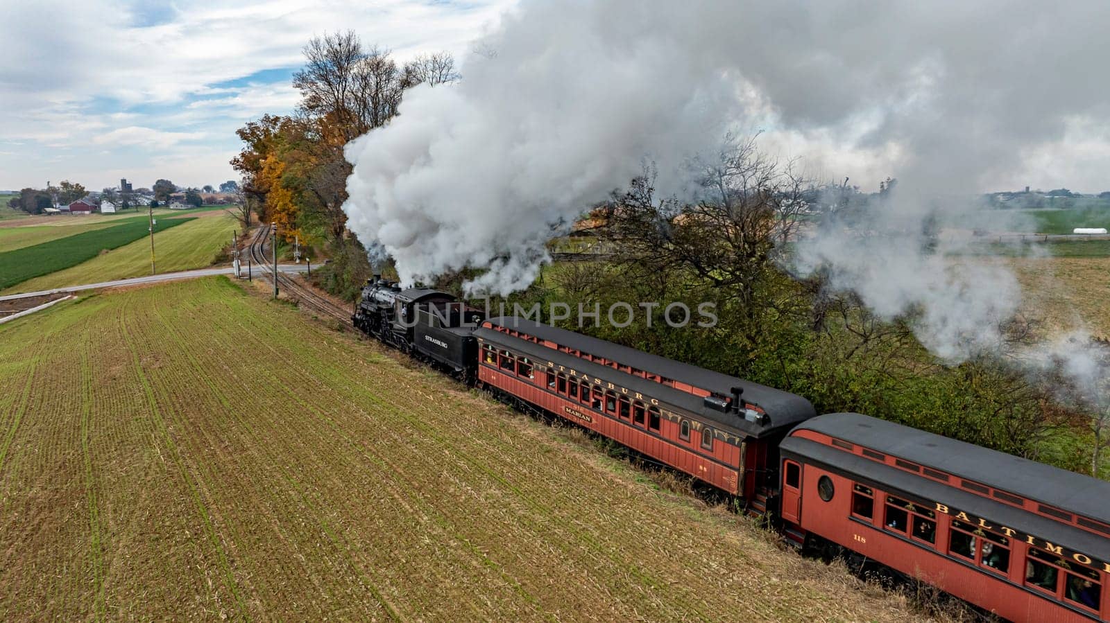 Ronks, Pennsylvania, USA, October 4, 2023 - A steam train chugs along a rural track, billowing smoke against a backdrop of fields and trees in autumn.