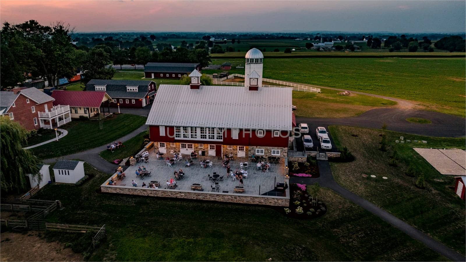 Ronks, Pennsylvania, USA, August 1, 2024 - People enjoy an outdoor gathering at a barn venue surrounded by green fields during sunset.