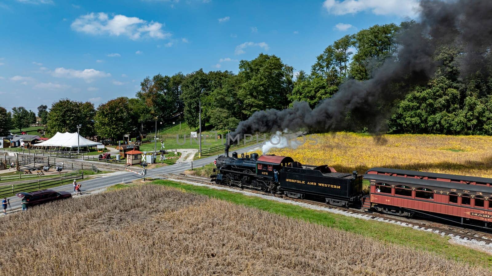 Ronks, Pennsylvania, USA, October 4, 2023 - A steam engine pulls a vintage train past a cornfield and fairground under a clear blue sky.