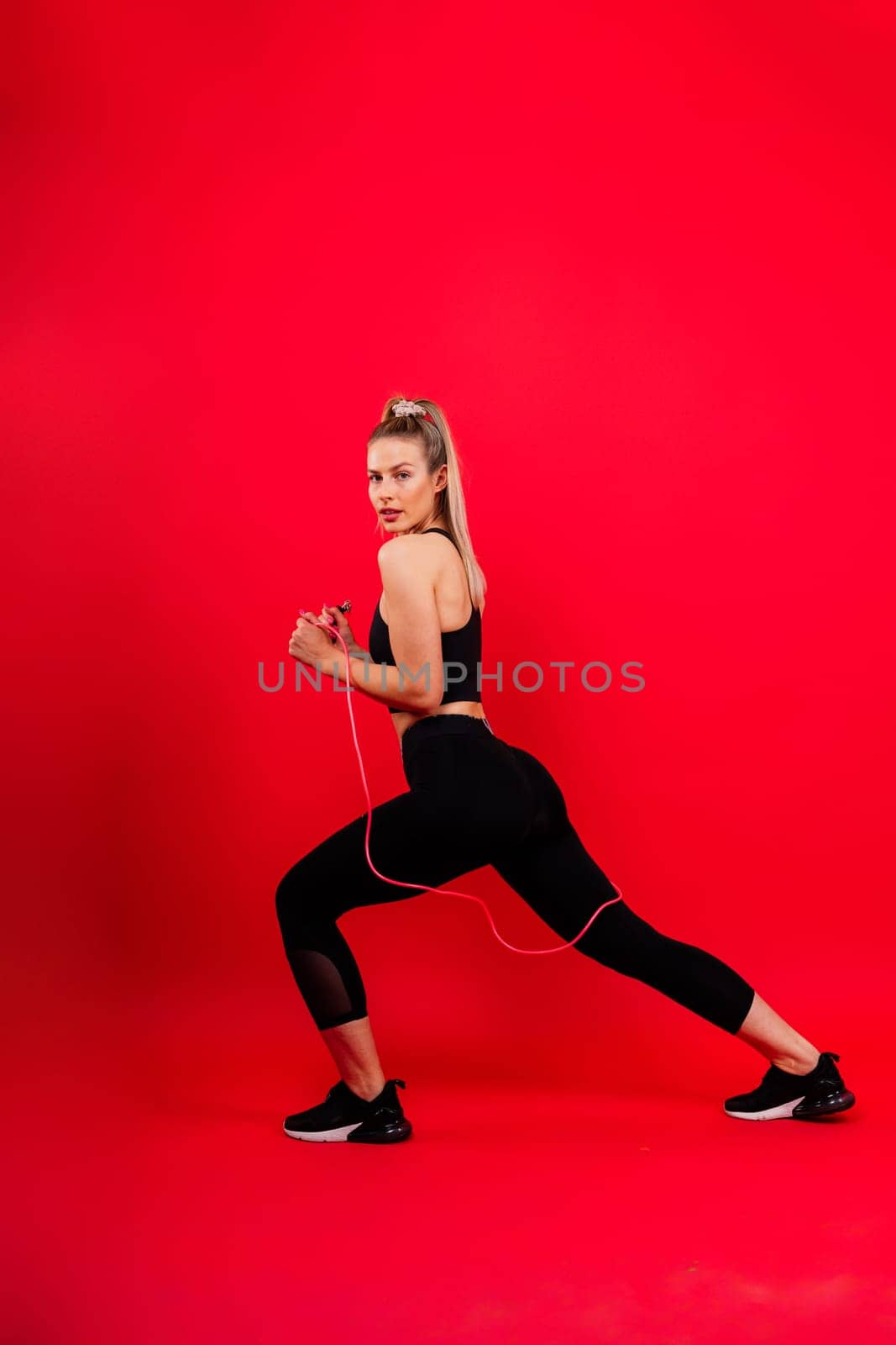 Fitness woman doing jumping exercises with a skipping rope on colorful yellow background.