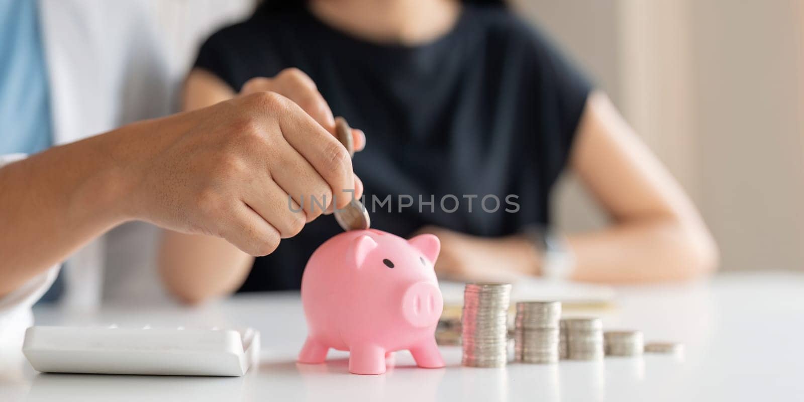 Family savings. Happy couple asian putting coin in piggybank while sitting together on desk at home, loving spouse planning budget and saving money for future by nateemee