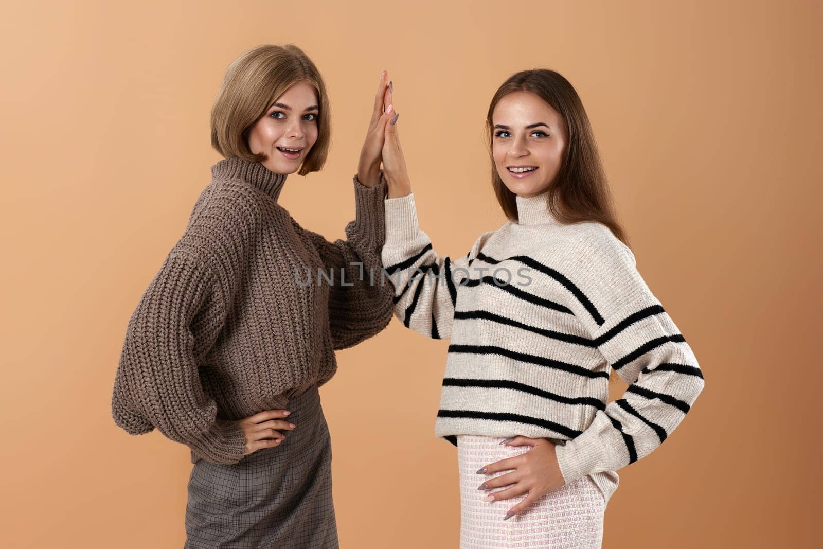 two young women friends giving high five hold hands on beige background