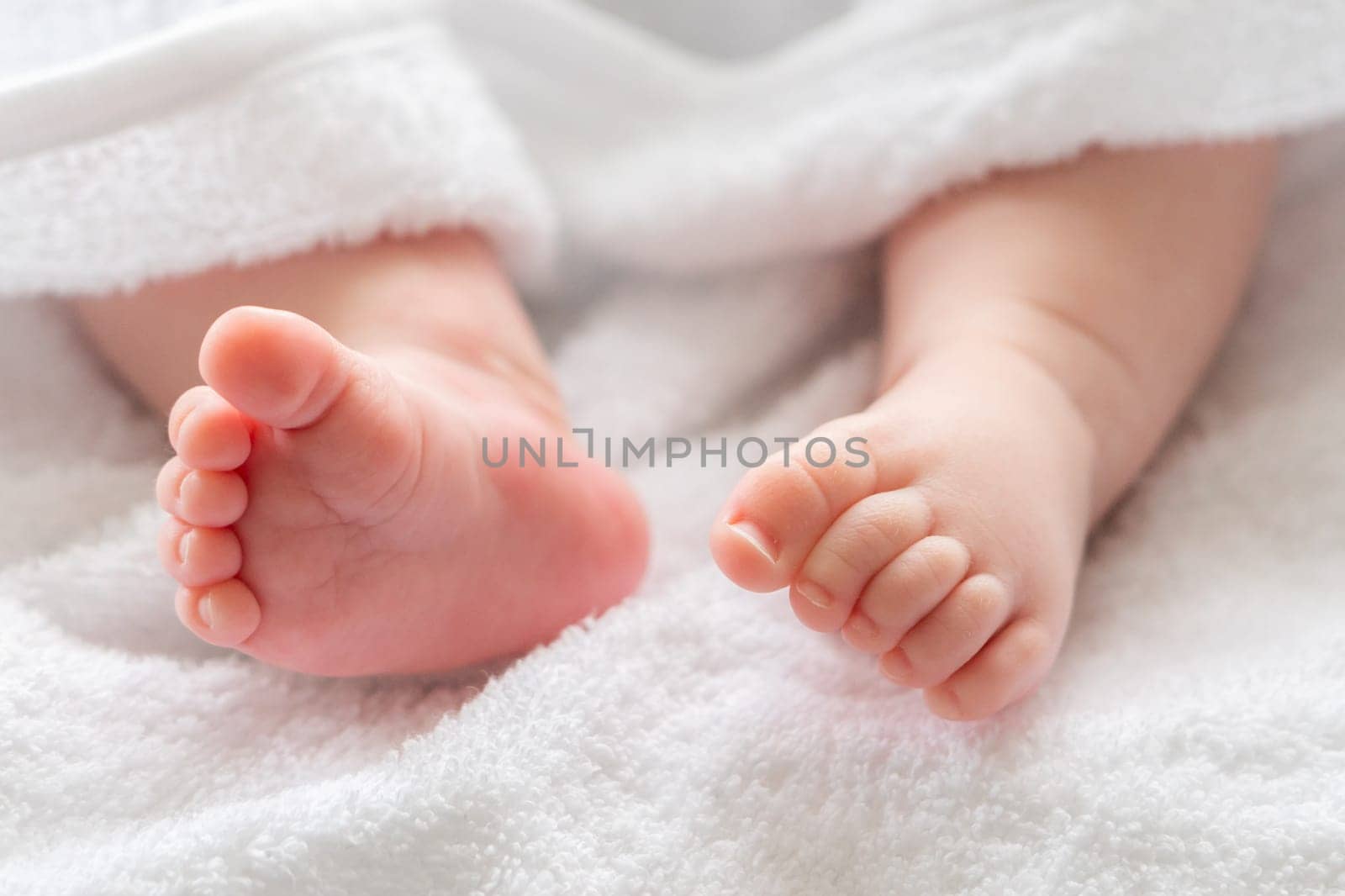 Beneath the luxurious softness of a white towel, an infant's feet and legs emerge, symbolizing gentle care after a bath