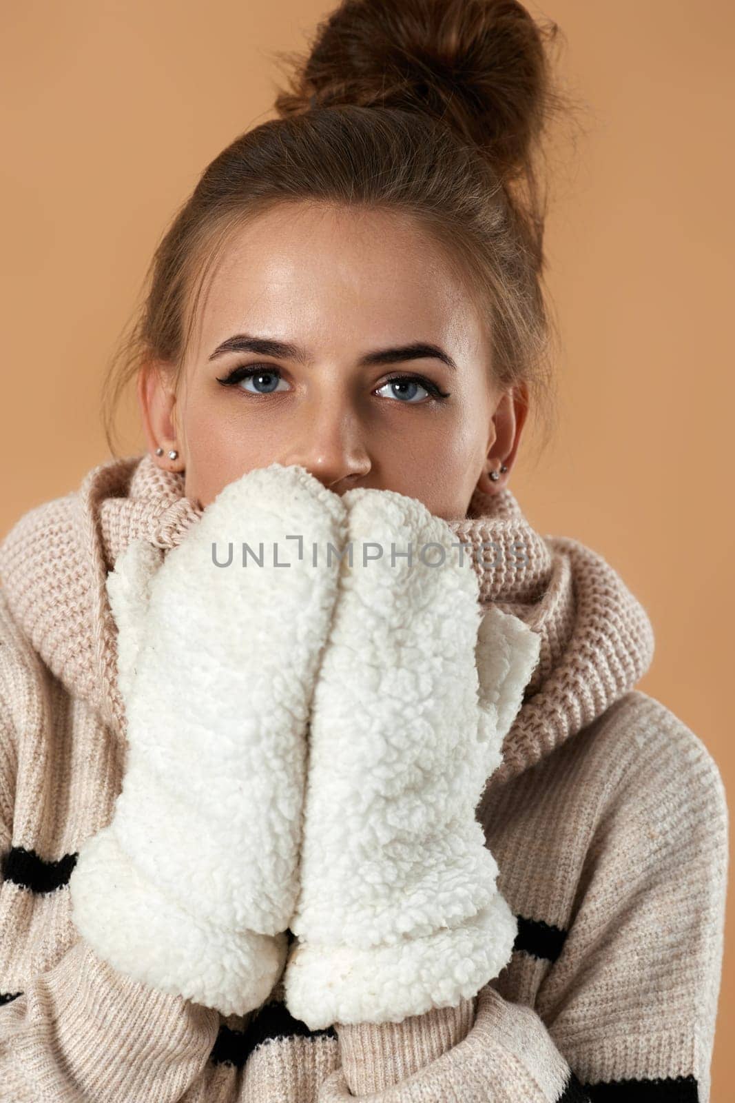 happy young woman in wool sweater and mittens on beige background