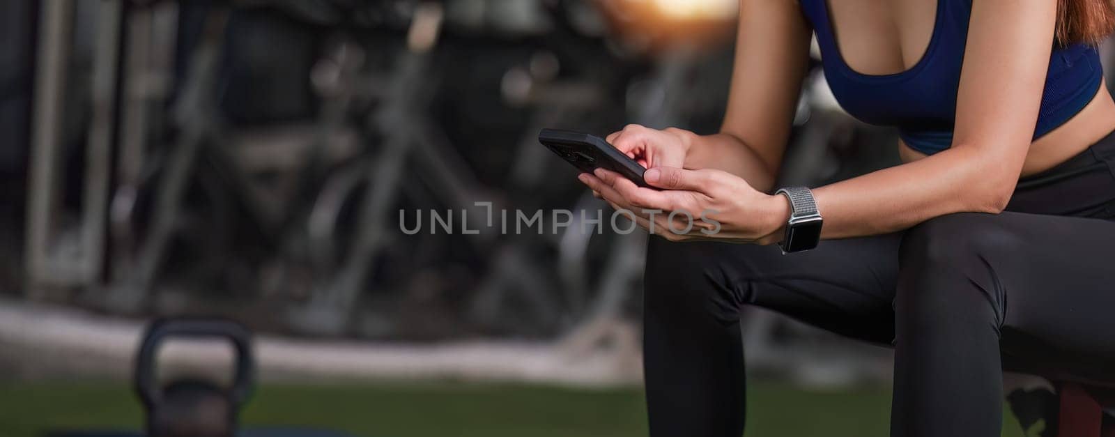 Young female athlete in sportswear sits at the gym using a cell phone while relaxing..