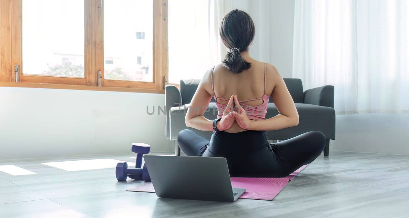 Young woman exercising in front of laptop Wear a sports bar outfit. Do yoga and lift dumbbells on the exercise mat..