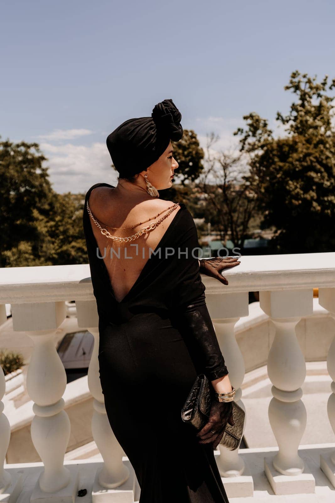 Stylish woman in the city. Fashion photo of a beautiful model in an elegant black dress posing against the backdrop of a building on a city street by Matiunina