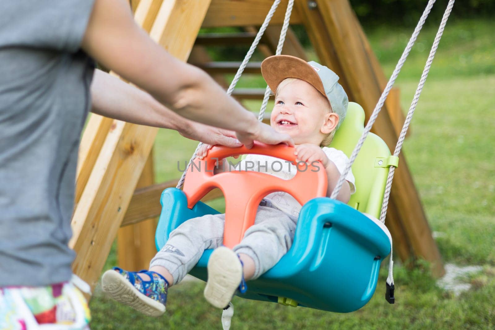Mother pushing her infant baby boy child on a swing on playground outdoors. by kasto