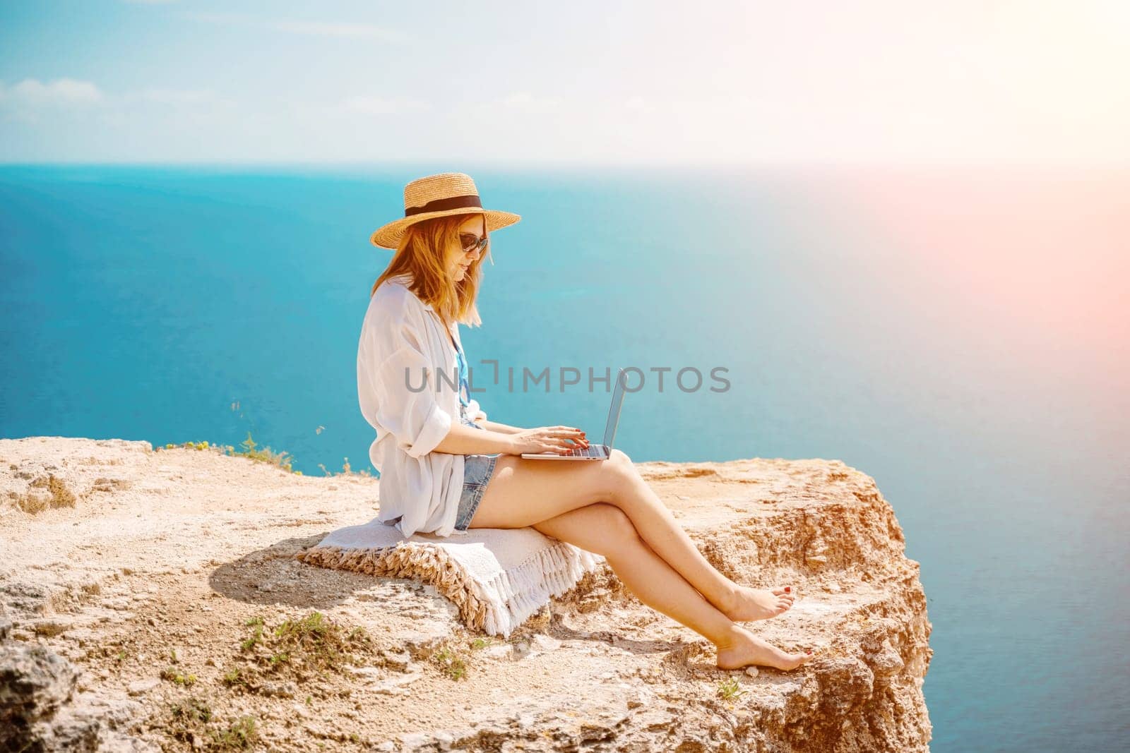 Freelance woman working on a laptop by the sea, typing away on the keyboard while enjoying the beautiful view, highlighting the idea of remote work. by Matiunina