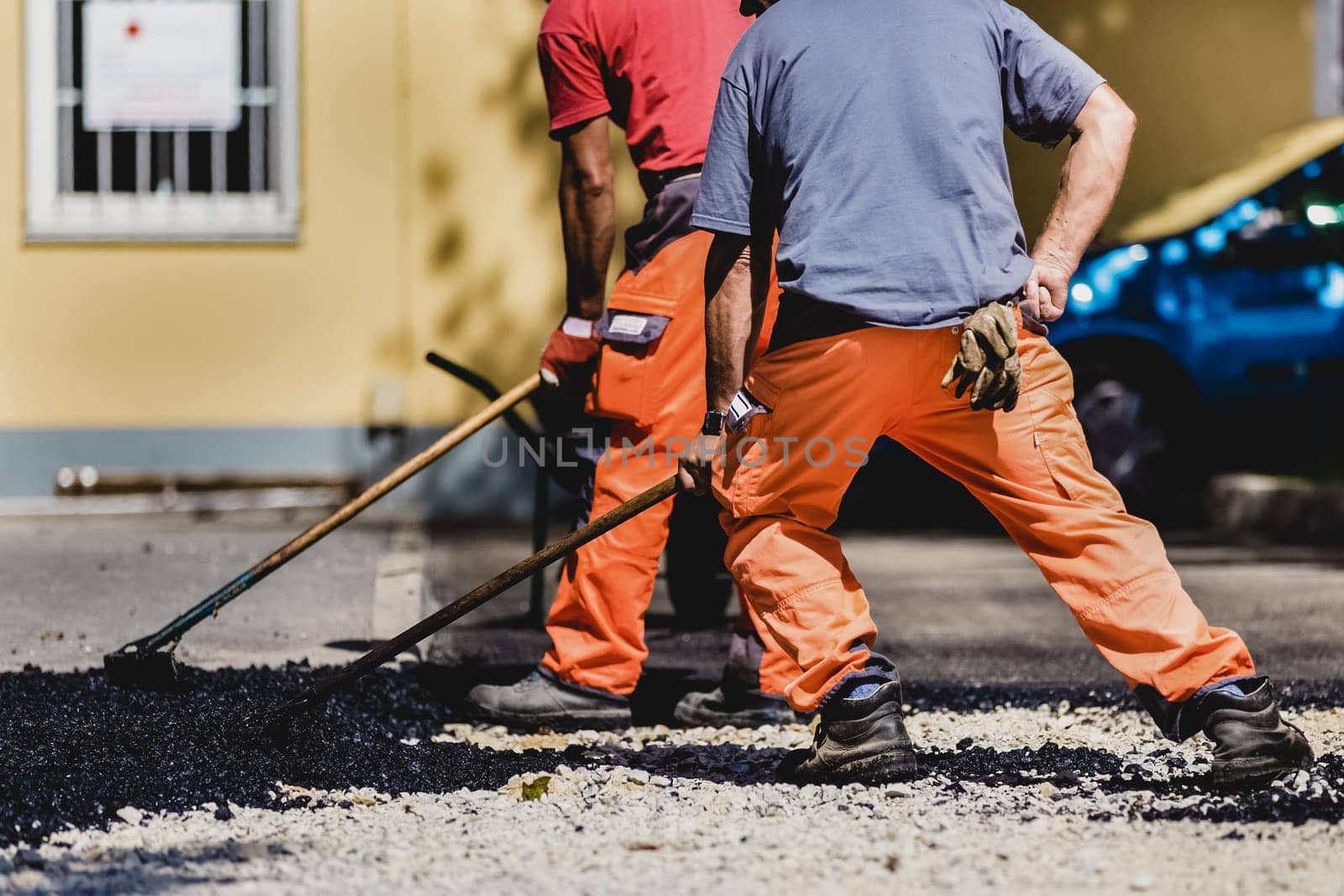 Construction workers during asphalting road works wearing coveralls. Manual labor on construction site.