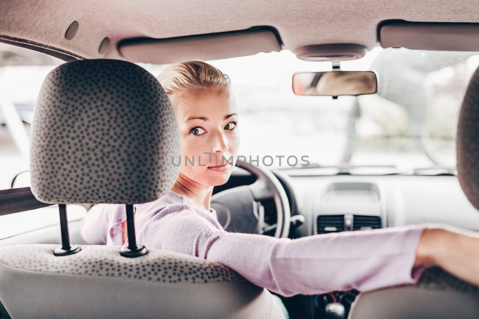 Female driver looking back while reversing in car. by kasto