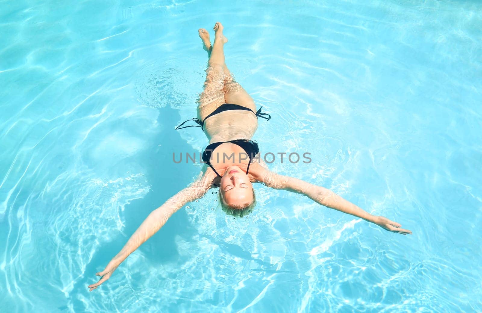 Beautiful Caucasian woman floating in turquoise blue swimming pool.