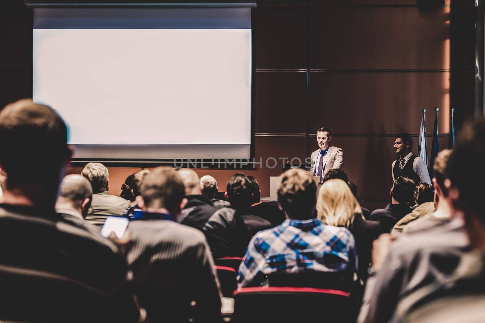 Speaker giving a talk in conference hall at business meeting event. Rear view of unrecognizable people in audience at the conference hall. Business and entrepreneurship concept.