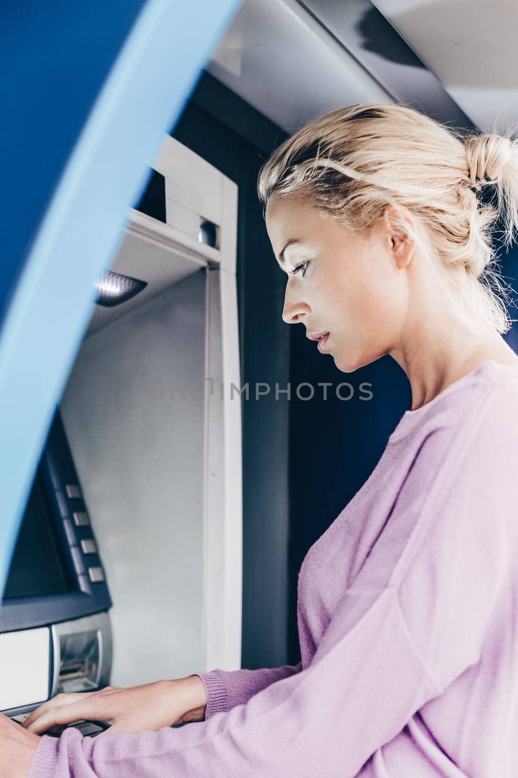 Young lady withdrawing money at ATM machine entering her pin code. by kasto