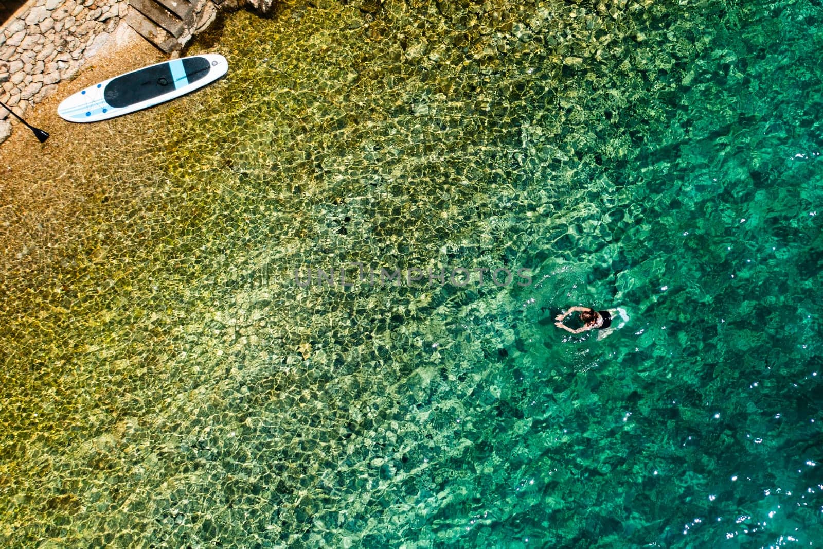 Woman swimming in clean, shallow sea water after SUP session.