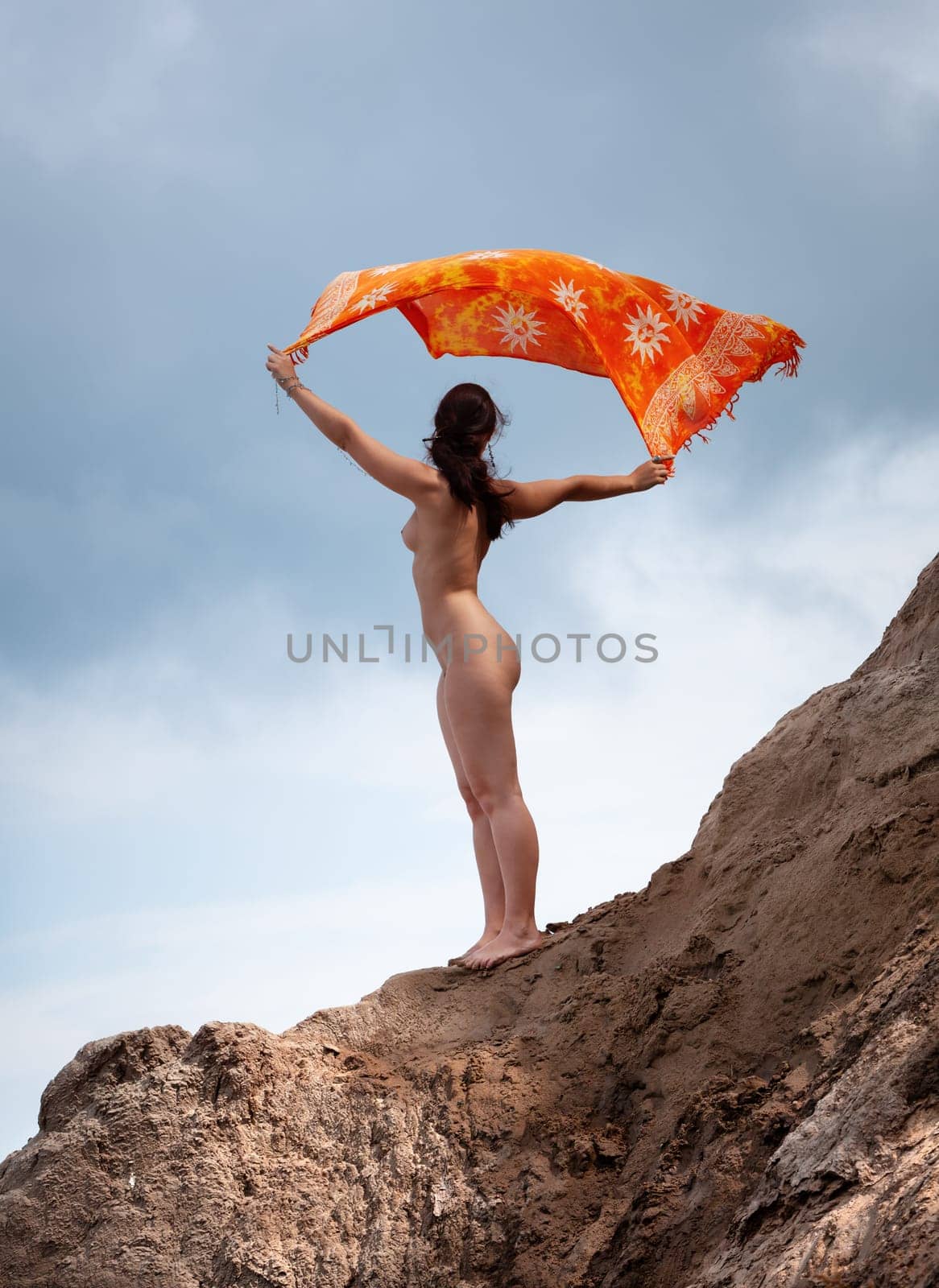 Young woman posing nude and enjoying nature on sand hill against sky background. Nature, beauty and nudity concept
