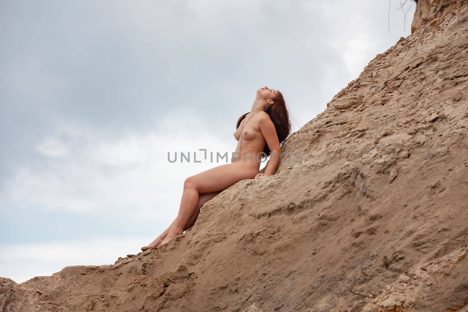 Young woman posing nude and enjoying nature on sand hill against sky background. Nature, beauty and nudity concept